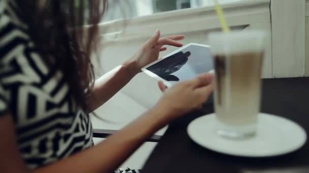 Girl dricka latte och arbetar med tabletten i café — Stockvideo