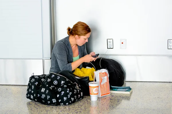 Woman seated on hte floor charging her phone in an airport — Stock Photo, Image