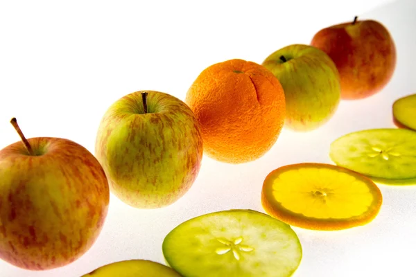 Line of apples and backlit slices with one orange — Stock Photo, Image