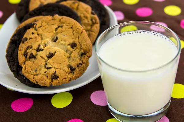 Gocce di cioccolato e biscotti al cioccolato intorno al bicchiere di latte — Foto Stock