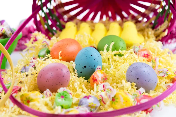 Osterkorb mit bunten Eiern, gelben Küken und Süßigkeiten — Stockfoto