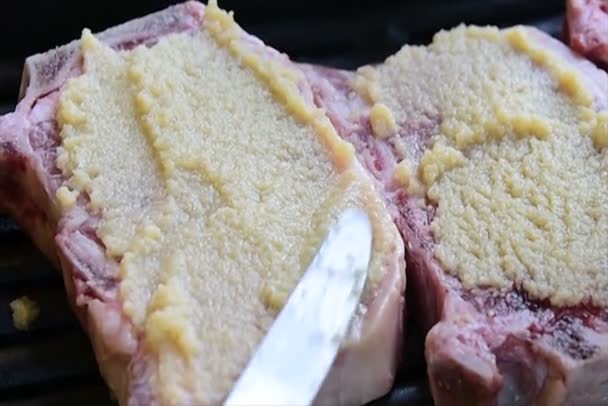 Spreading garlic for garlic encrusted steaks while they are sizzling on the grill — Stock Video