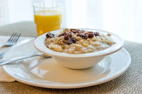 Juice and a bowl of oatmeal with almond slices and raisins — Stock Photo, Image