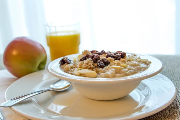 Juice and a bowl of oatmeal with almond slices and raisins — Stock Photo, Image