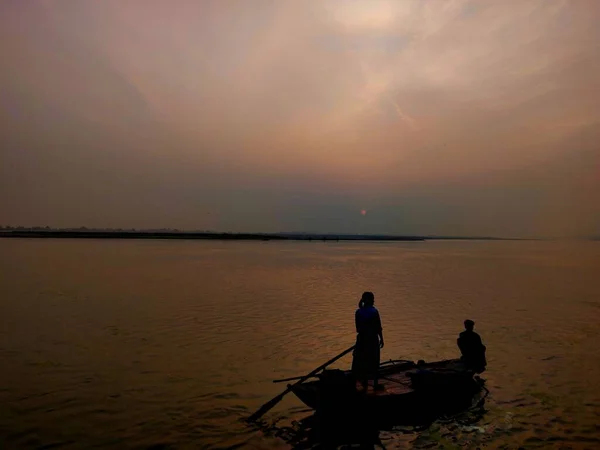 İnsanlar şafak vakti Ganga nehrinde teknede balık tutuyorlar.
