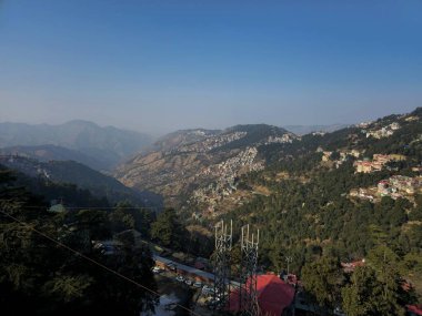Shimla vadilerinin geniş panoramik manzarası ve evlerle benekli orman tepeleri, aydınlık bir günde çekilmiş yükseklik, derinlik ve doğal hatları vurgulayan.