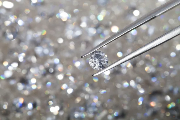 Diamante tenuto da pinzette da vicino. più diamanti fuori fuoco in — Foto Stock