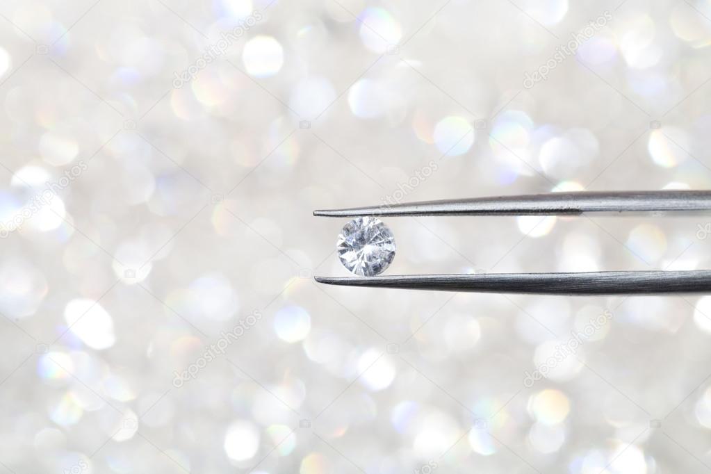 diamond held by tweezers close up. more diamonds out of focus in