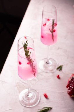 Beyaz bir masada iki bardak pembe nar limonatası.