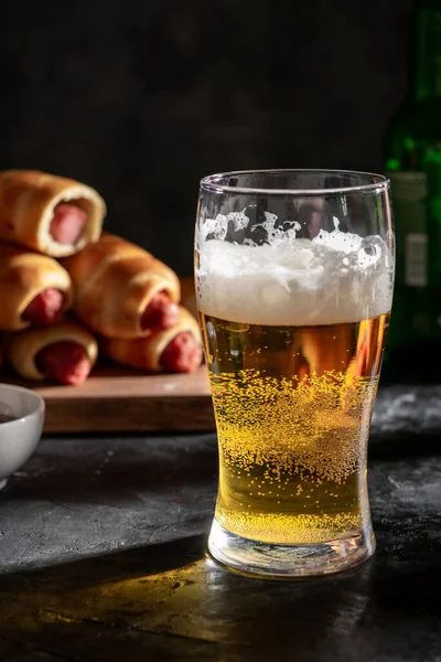 A big glass of light beer and sausages in the dough on the board