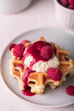 Taze pişmiş waffle, ahududu şurubu ve tabakta dondurma.