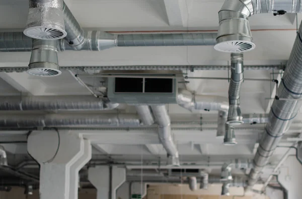 Air duct and air conditioner pipe on white ceiling wall. Ventilation system on the ceiling of large building. Air condition and hvac system installation under bareskin ceiling before interior finishing.
