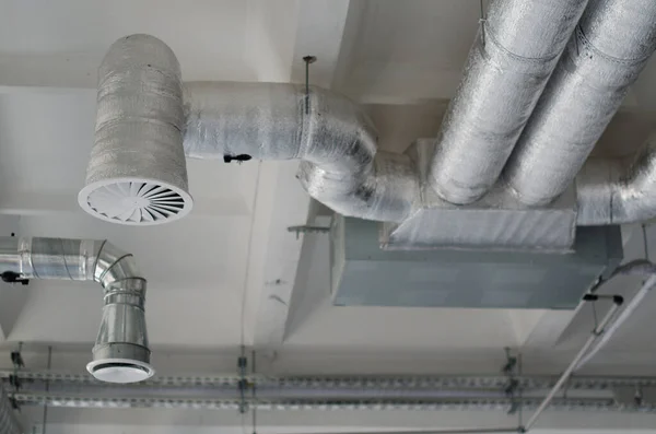 在新建筑物的天花板上悬挂着银质绝缘材料中的通风管 工业用通风管系统 空气流动和通风系统 — 图库照片