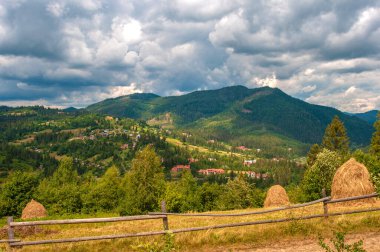 Karpatlar 'ın üzerinde resimli bulutlar. Dağ manzarası. Vadideki köy. Bir saman yığını. Uzakta sis var..