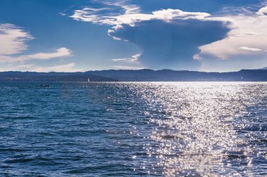 İtalya. Garda Gölü 'nde akşam. Su üzerinde güneşli bir yol. Resimli bulutlar güneş ışınlarıyla aydınlatılır..
