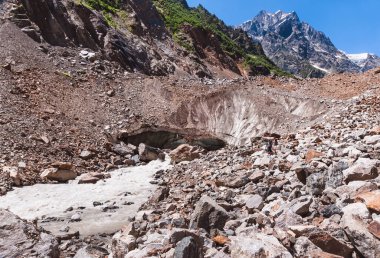 Georgia mı? Yaz günü. Chalaadi buzulu. Önde taşlar, arkada dağlar. Parlak mavi gökyüzü..