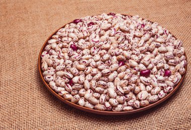 Kil tabakta olgun fasulye tohumu. Kırmızı damarlı beyaz mermer fasulye. Çuval bezi arkaplanı..