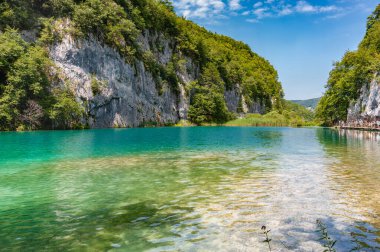 Hırvatistan. Plitvice Gölleri Ulusal Parkı. Beyaz bulutlu mavi gökyüzü. Dağlar ve bitki örtüsü arasında şeffaf göl suyu..