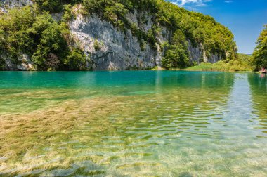 Hırvatistan. Plitvice Gölleri Ulusal Parkı. Beyaz bulutlu mavi gökyüzü. Dağlar ve bitki örtüsü arasında şeffaf göl suyu..