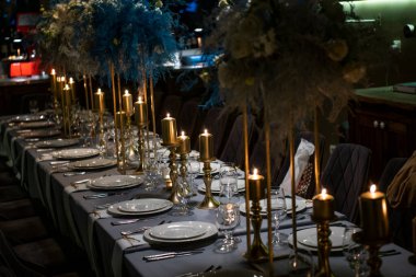 Altın detaylar, mumlar ve arka planda loş ışıklarla süslenmiş zarif bir masa.