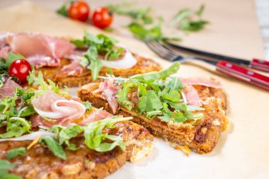 Arugula, prosciutto ve vişneli domatesli sağlıklı kabaklı pizza.