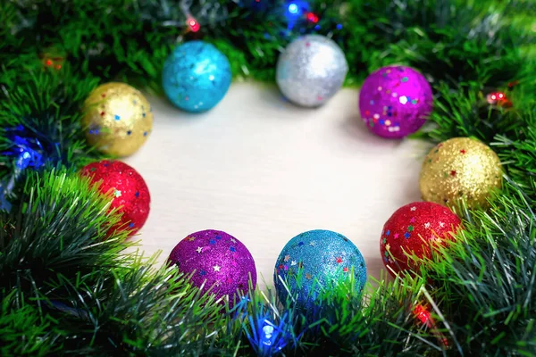Selective and soft focus of multi-colored shiny Christmas tree balls on wreath of green tinsel and burning electric lights on garland. New year\'s background and postcard. Holiday home decoration