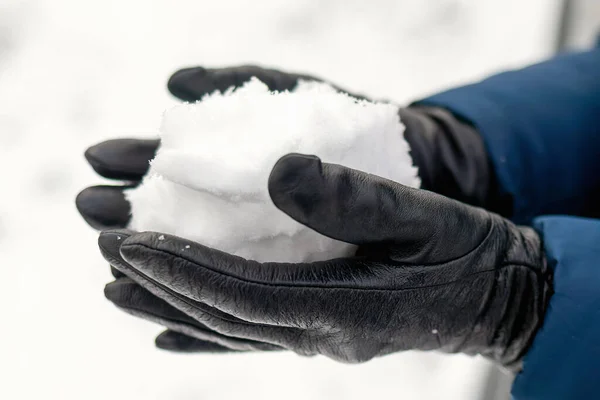 Close-up of snow in hands of woman in leather gloves. Concept of weather and snowfall forecast. Walk outdoor and winter games. Protection of skin of hands during cold weather with creams
