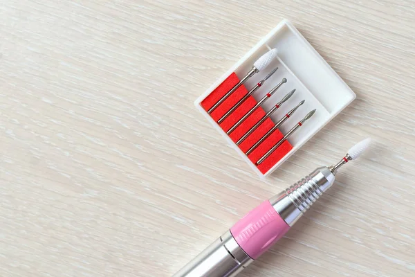 Top view of set of diamond cutters in box and metall pen with ceramic bit for professional manicure on a light wooden background. Specialized equipment for nail service masters. Copy space