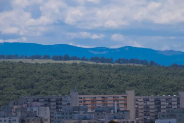 Arka plandaki dağlar ve bulutlar bir mahalledeki tepe ve doğu Avrupa binalarıyla çevrili..