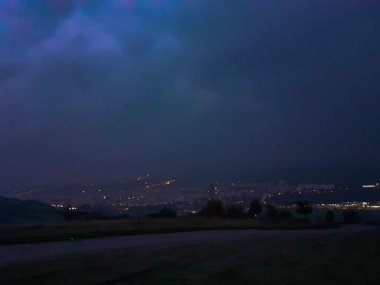 Şehrin üzerinde bulutlu ve sisli bir akşam, tepenin manzarası, şehrin ışıkları.