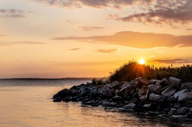 Sakin bir nehir ya da göl üzerindeki güzel günbatımının resmedilmiş görüntüsü. Gökyüzünde bulutlar ve uzaklarda sazlıklar olan bir yaz akşamı..