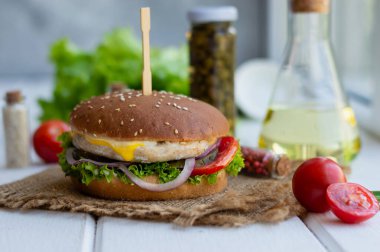 Beyaz ahşap bir yüzeyde tavuk pirzolası, peynir, soğan, marul yaprağı ve domatesli geleneksel beyaz susamlı hamburger var. Gıda ile güzel bir arkaplan, bir parça metin ekleme yeteneği.