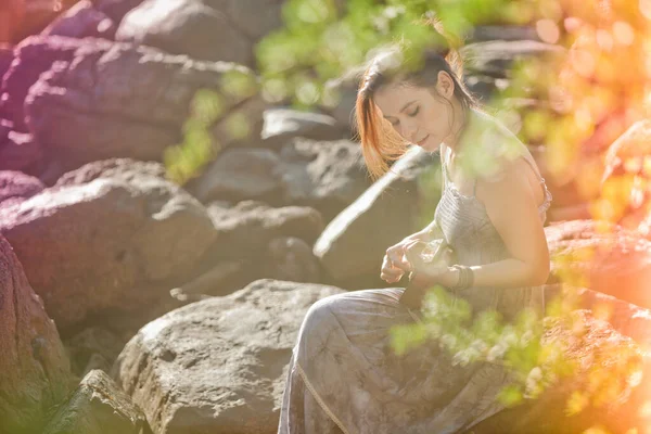 Güneş ışığı kumsalında ukulele çalan kadın.