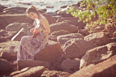 Güneş ışığı kumsalında ukulele çalan kadın.