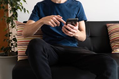 Genç adam koltuğunda oturmuş, akıllı telefonuyla oynaşıyor..