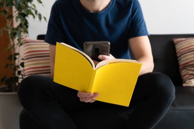 Kitap arkasında akıllı telefonunu kullanan tanınmayan bir adam. Teknoloji ve edebiyat kavramı. 