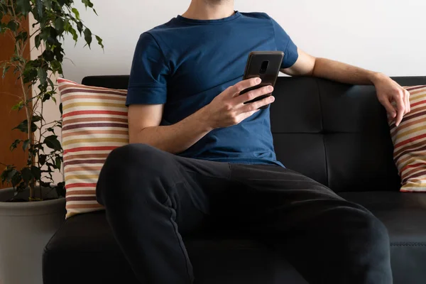 Young man relaxed on the couch at home using his smartphone.