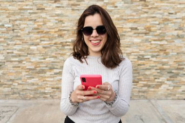 Genç bir kadının gülüşü ve akıllı telefon kullanışı ön planda.. 