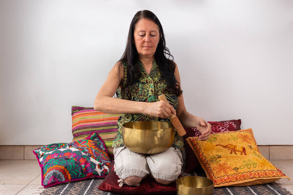 Женщина средних лет с помощью тибетской чаши для пения создает расслабляющую и дзен-ауру.