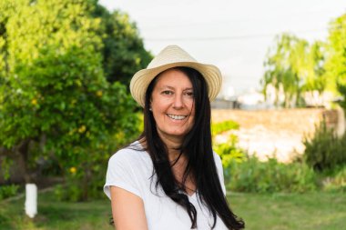 Evinin bahçesindeki orta yaşlı kadın kameraya mutlu bir şekilde gülümsüyor..