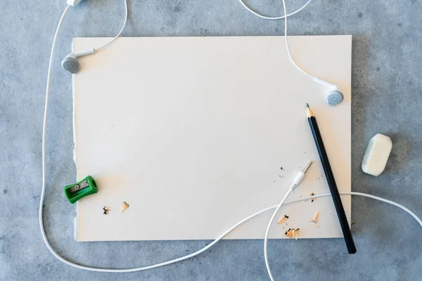 White drawing sheet with sharp black pencil and earphones.