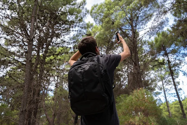 Young man lost in a forest and looking for a signal on his phone