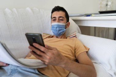 Tecritteki genç adam cep telefonuyla kanepede yatıyor..