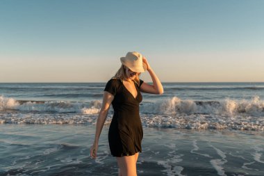 Genç ve güzel bir kadın, deniz kıyısında günbatımının tadını çıkarıyor.