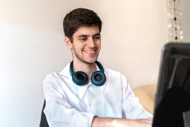 Ofisteki genç adam gülümseyerek bilgisayarda yazıyor.