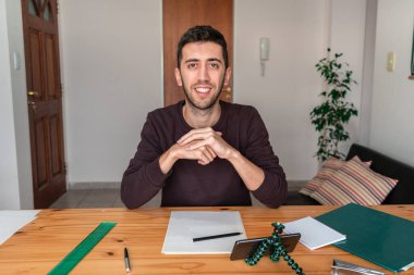 Evde gülümseyen ve kameraya bakan çevrimiçi öğrenci.