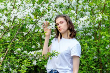 Bahar yürüyüşü. Bir kız çiçek açan bir elma bahçesinde yürüyor.