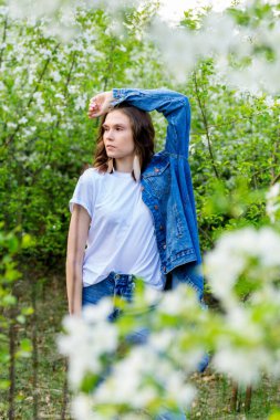 Bahar yürüyüşü. Bir kız çiçek açan bir elma bahçesinde yürüyor.