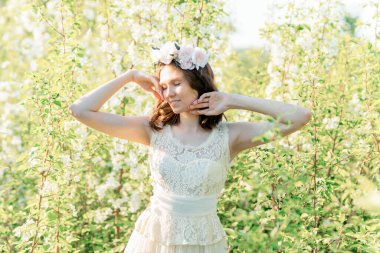 Çiçekli bir çelengin içindeki güzel bir kız çiçek açan elma ağaçlarının arasında.