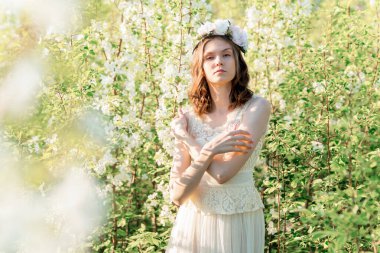 Çiçekli bir çelengin içindeki güzel bir kız çiçek açan elma ağaçlarının arasında.